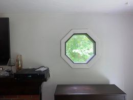 An octagonal window centered on a light-colored wall above a dark wooden piece of furniture.
