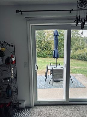 A glass sliding door looks out onto a patio with a blue umbrella, a table, and chairs on a blue patterned rug.