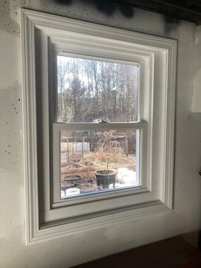 A white window with decorative molding, installed in an unfinished wall with visible joint compound.