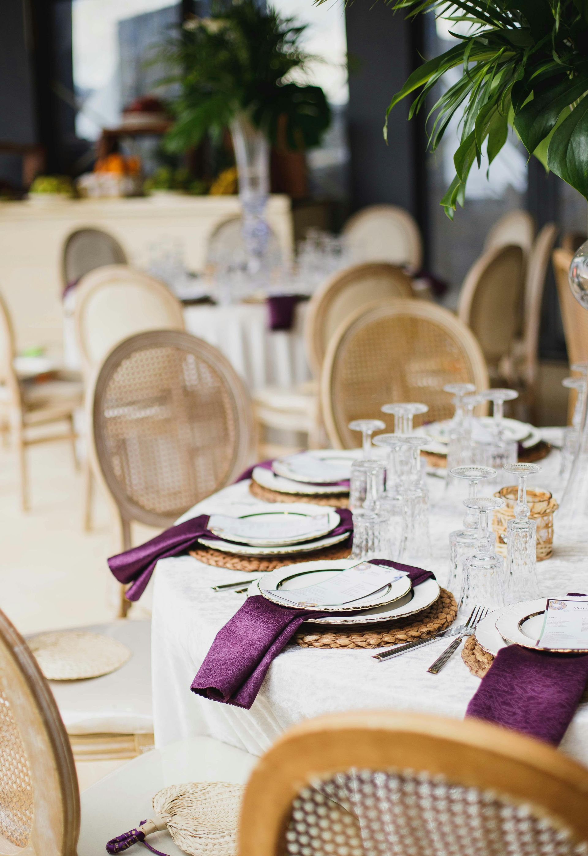 Intimate wedding table setup featuring rustic woven chairs, white linens, and purple napkins