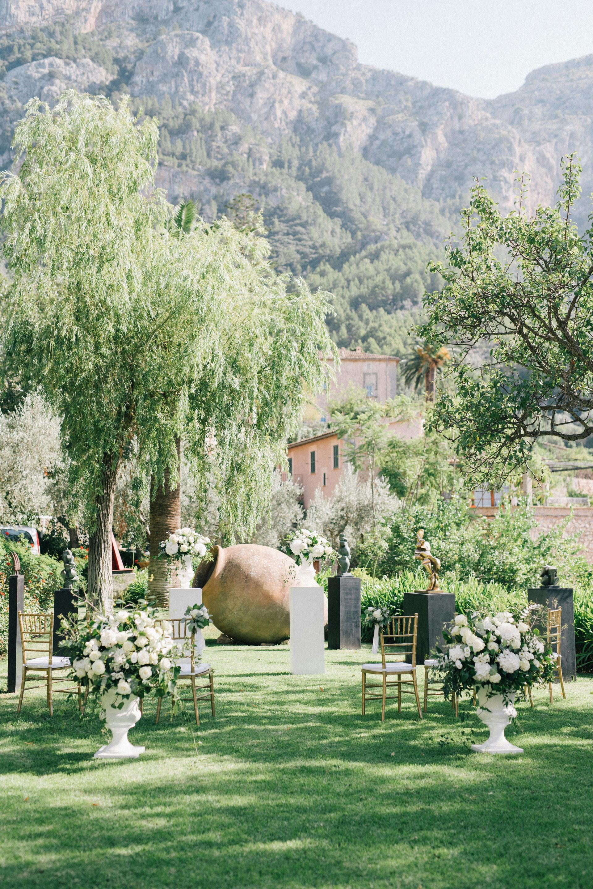 Outdoor wedding ceremony with white chairs and circular arch surrounded by greenery and mountains