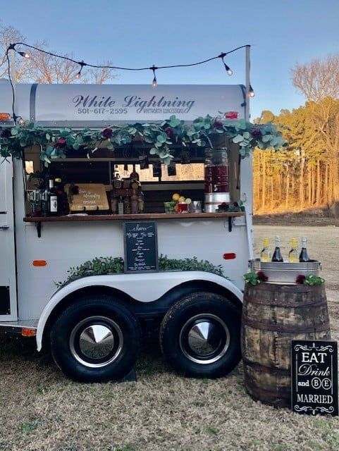 A white food truck is parked in a field next to a barrel.
