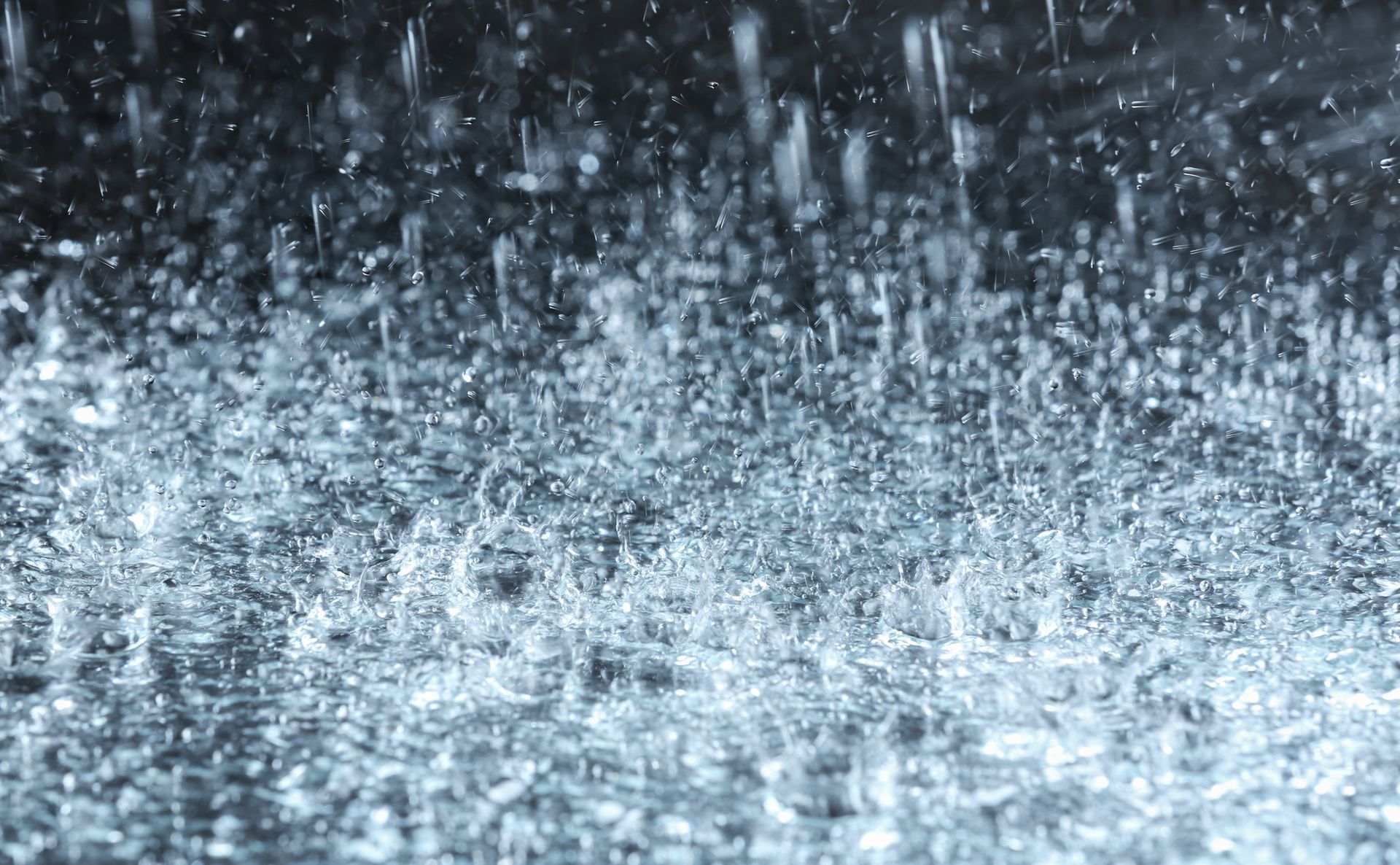 A close up of rain falling on a black surface.