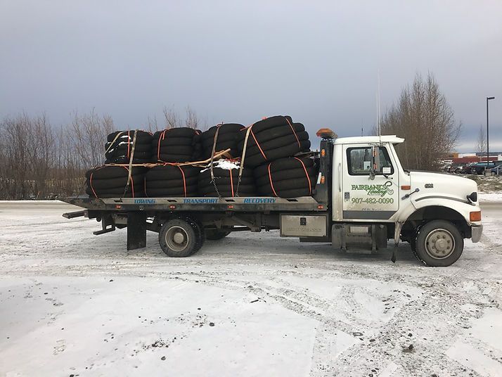 A tow truck filled with tires is parked in the snow.