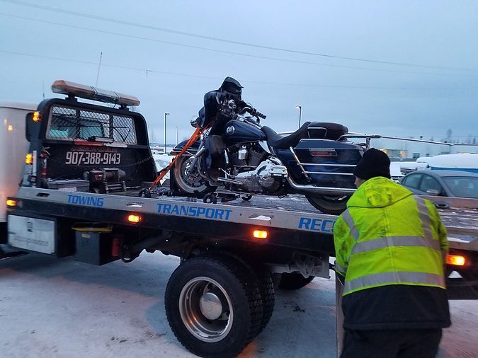 A motorcycle is being towed by a tow truck in the snow.