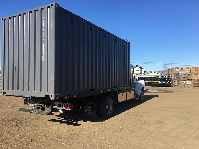 A large shipping container is on the back of a tow truck.