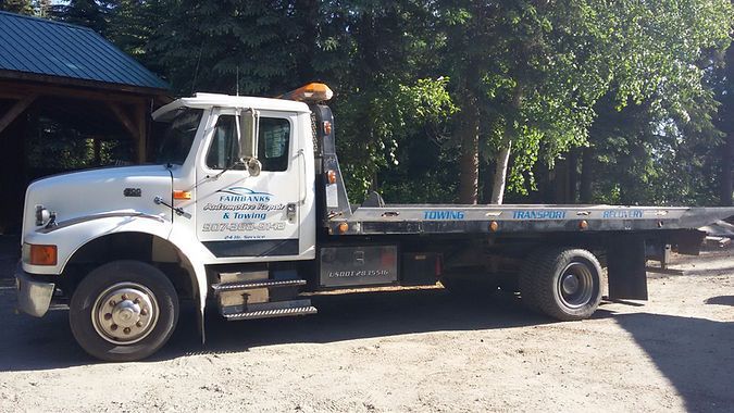 A white tow truck is parked in a gravel lot