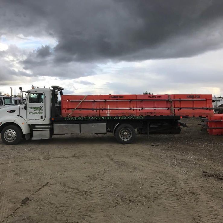 A white truck with an orange bed is parked in a dirt lot.