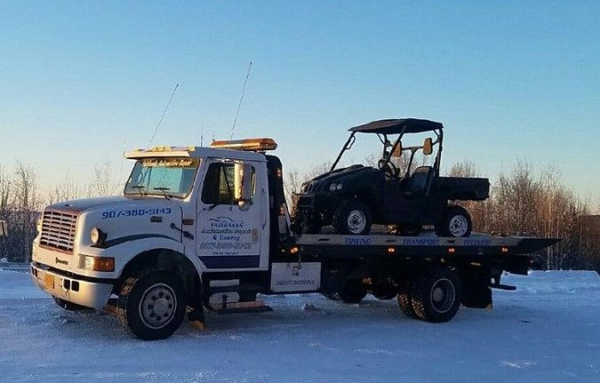 A tow truck is carrying a four wheeler in the snow.