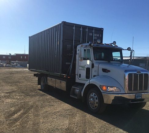 A semi truck with a container on the back is parked in a dirt lot.