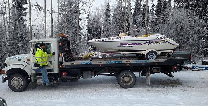 A tow truck is carrying a jet ski on the back of it.