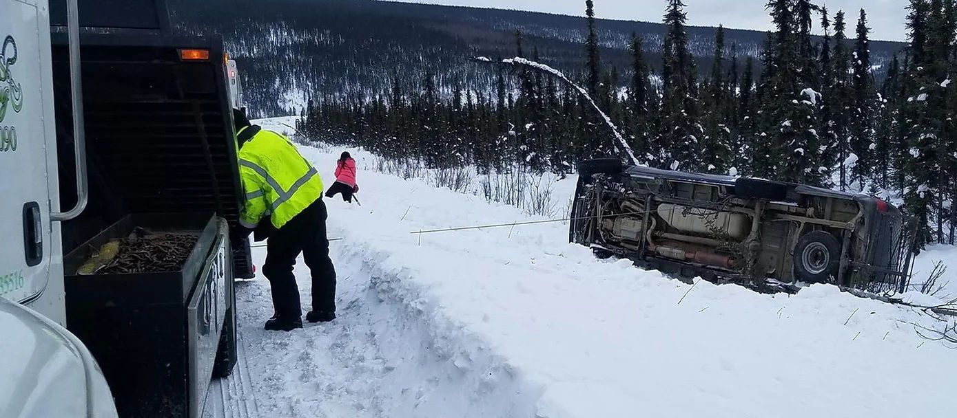 A man in a yellow vest is standing next to a truck in the snow.