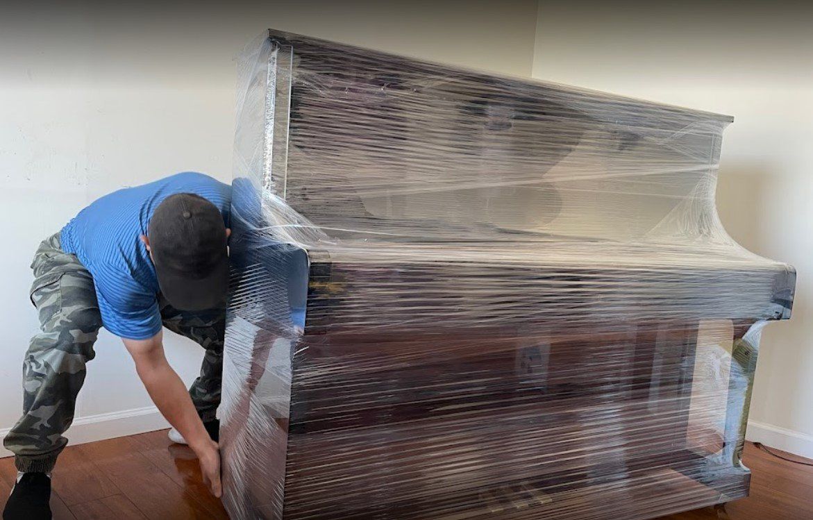 A man is wrapping a piano in plastic wrap.