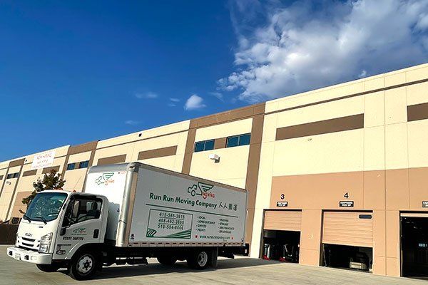 A white moving truck is parked in front of a large building.