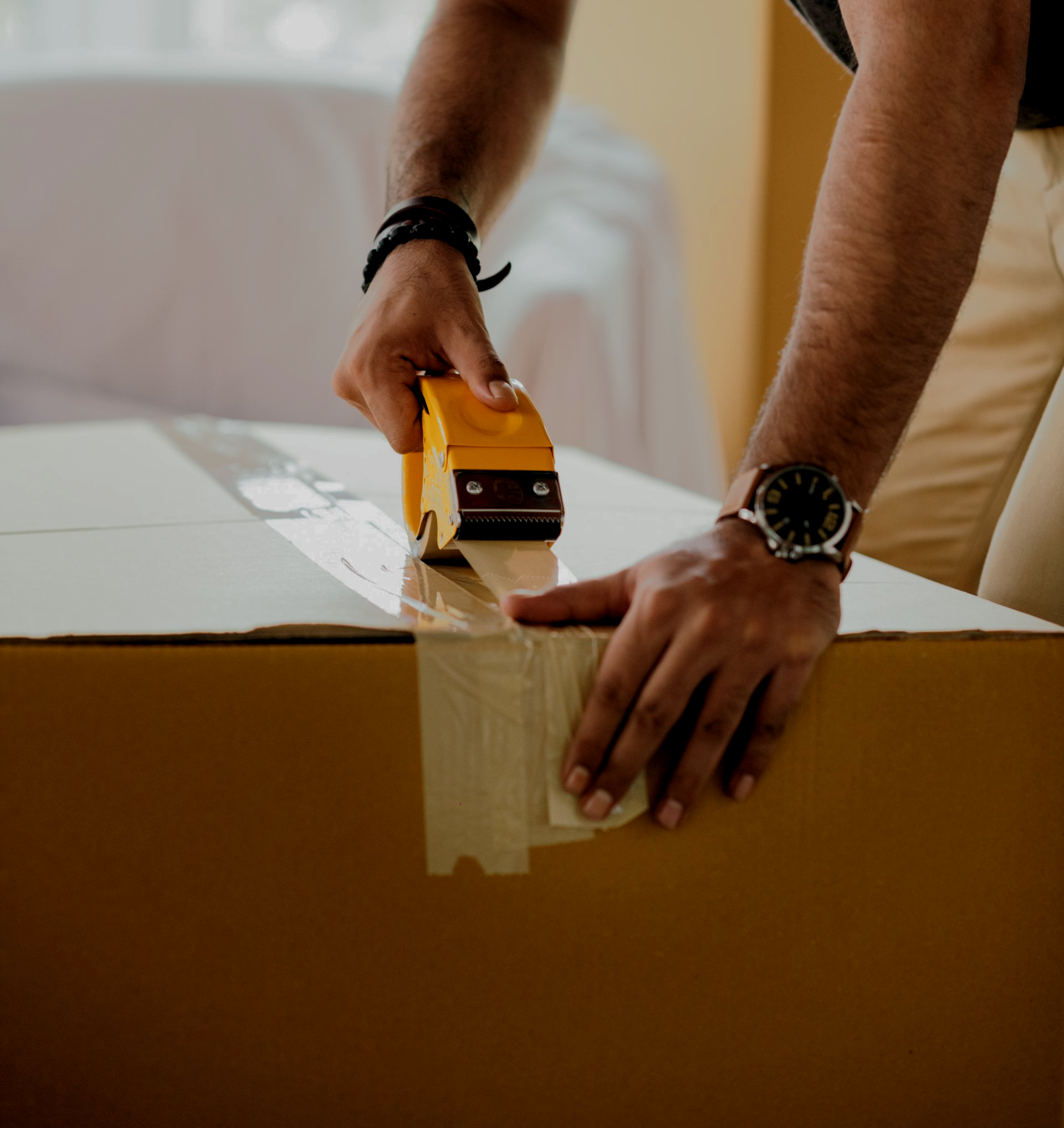 一名戴着手表的男子正在用胶带包裹一个纸箱