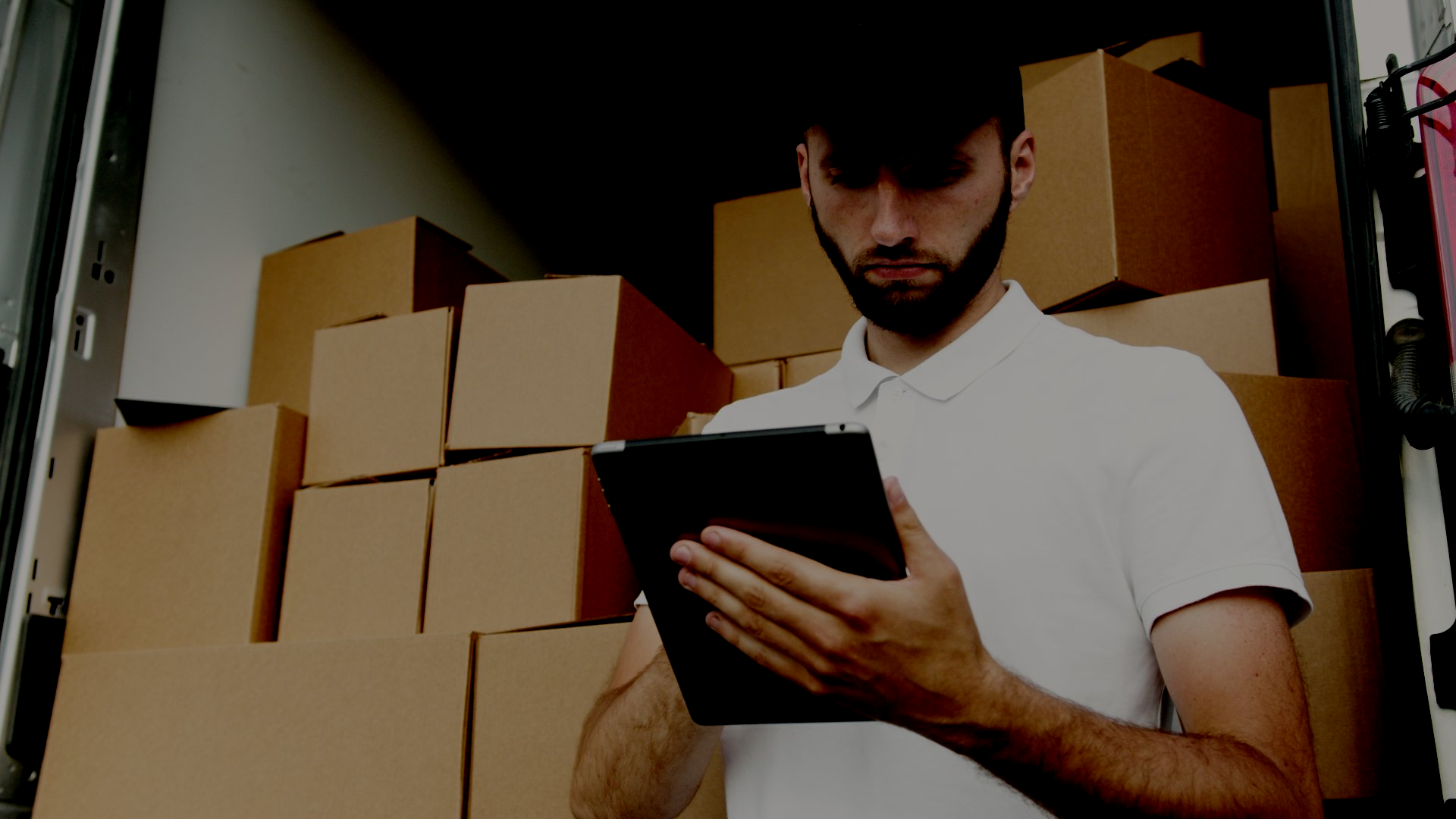 一名男子正在一辆装满纸箱的卡车前使用平板电脑。
