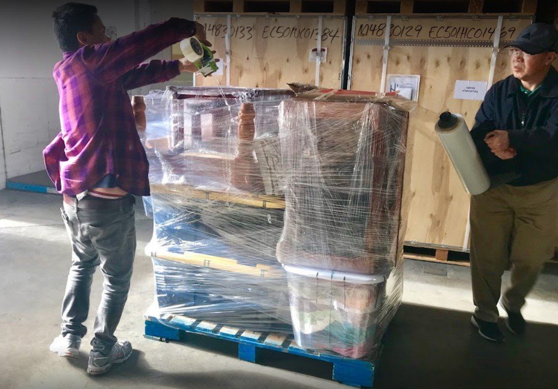 Two men are wrapping boxes on a pallet in a warehouse.