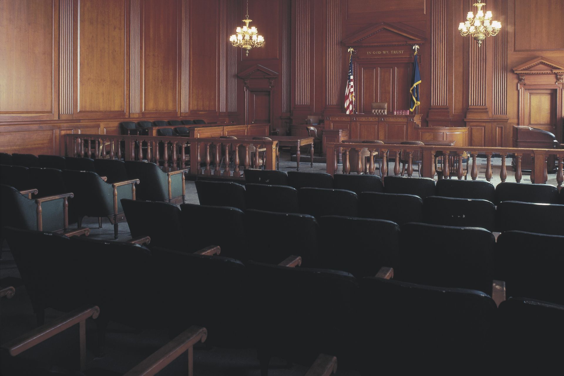 An empty courtroom with wood paneling and black seats.