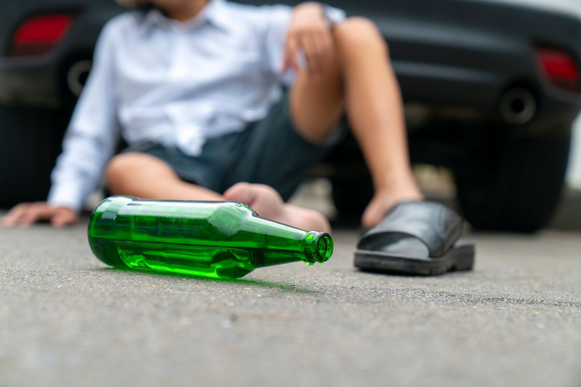 A man is sitting on the ground next to a bottle of beer.
