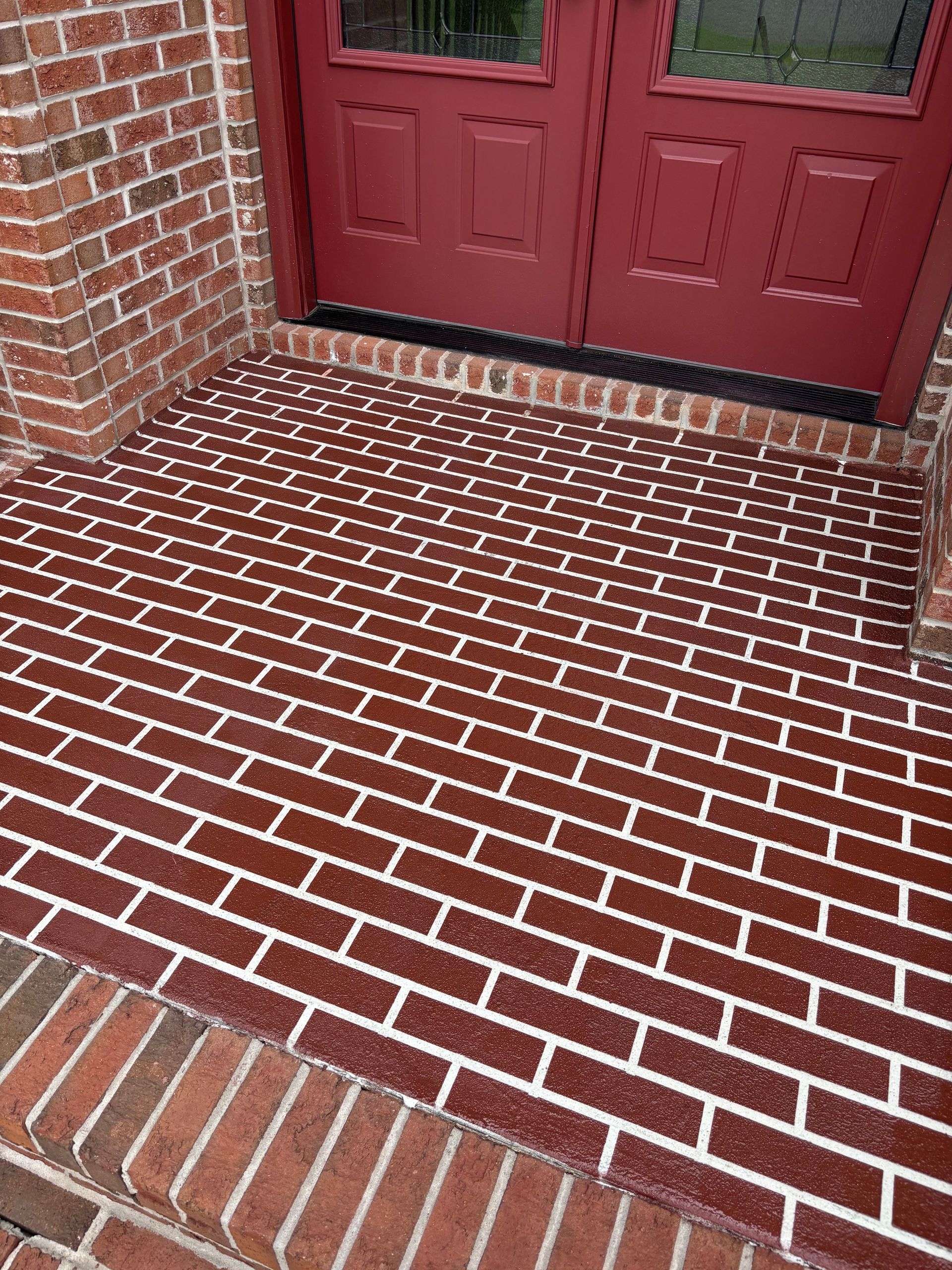 A red brick porch with a red door in the background.