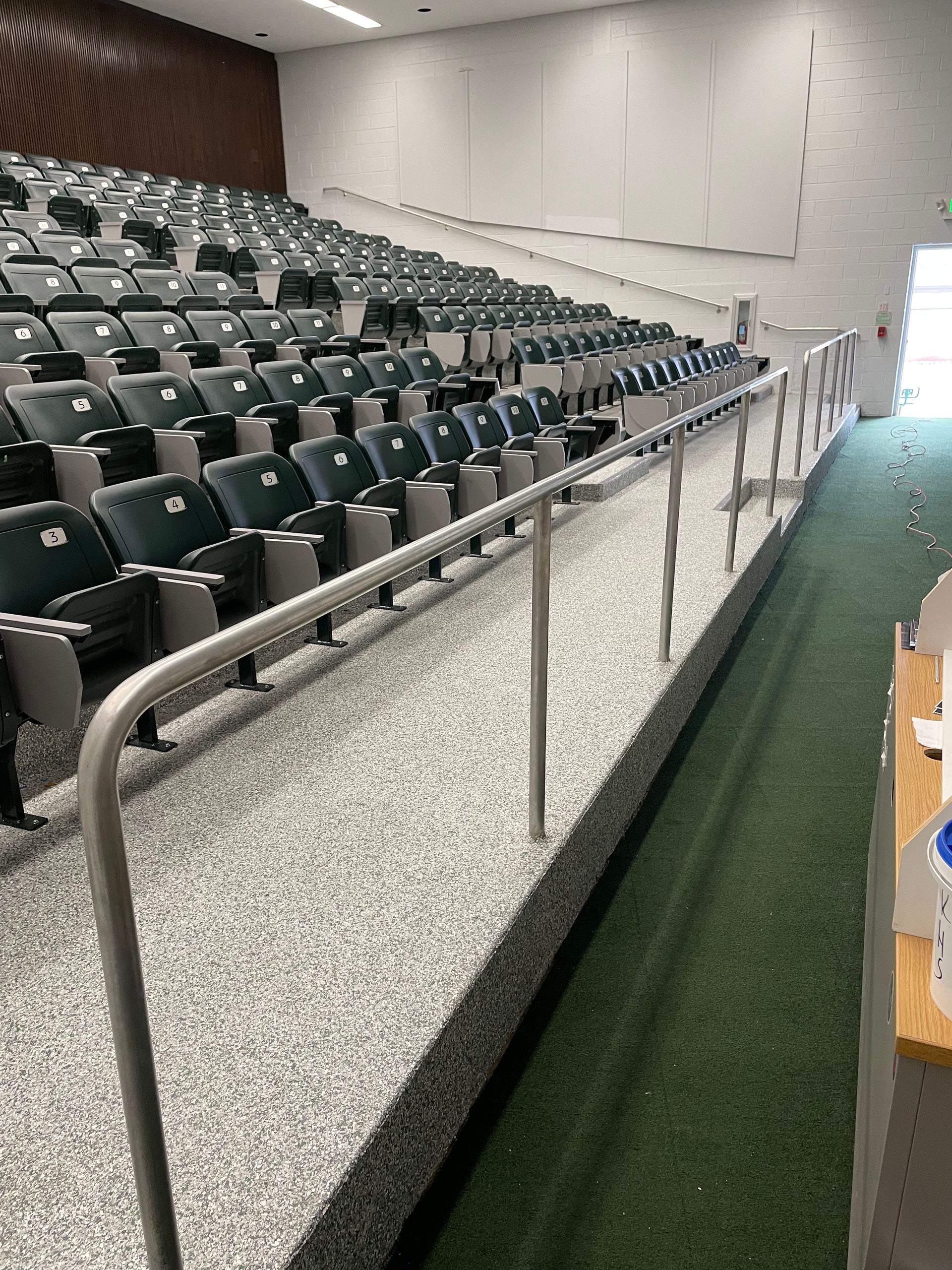 A row of empty seats in an auditorium with a metal railing.