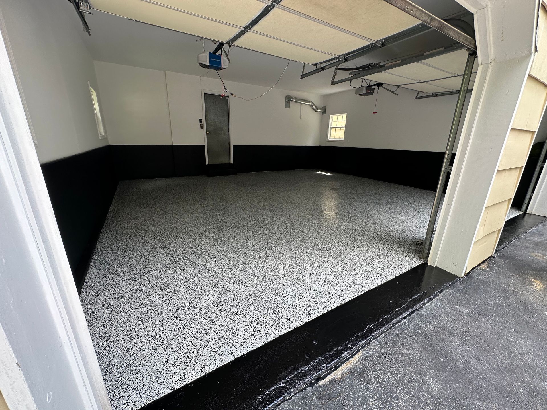A garage with a black and white floor and a garage door open.