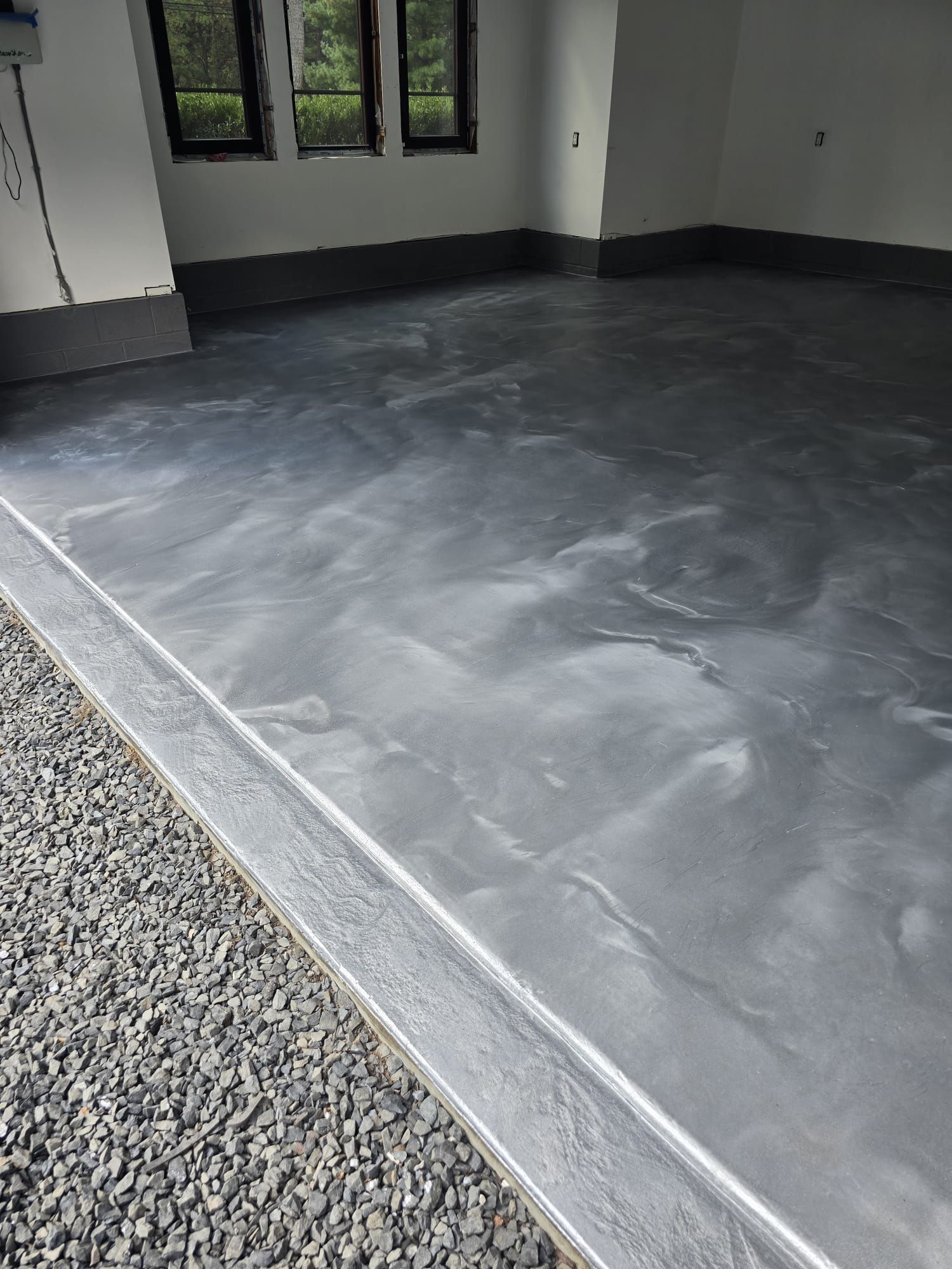 A gray metallic floor in a garage with gravel in the corner.