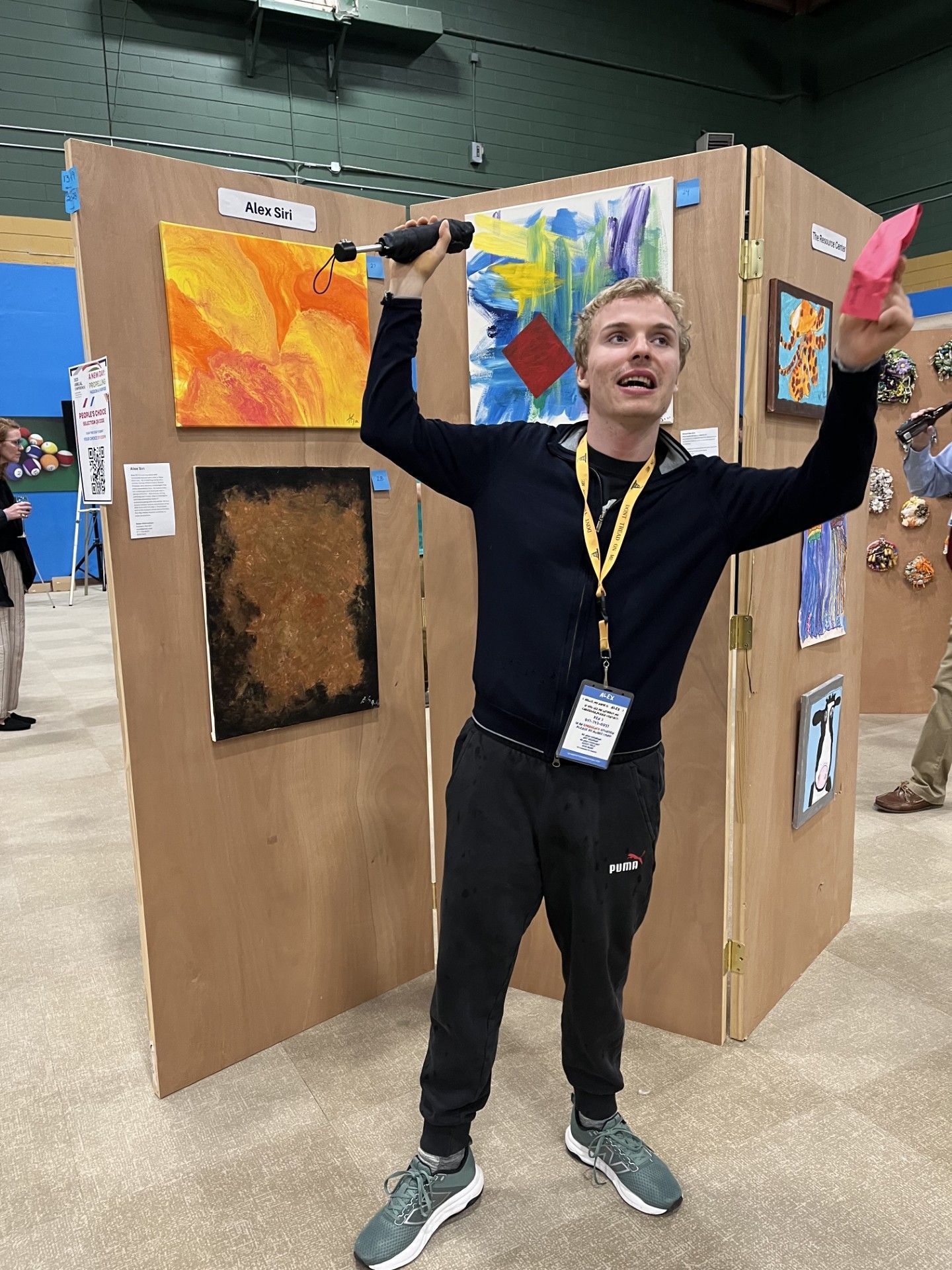 Man celebrating artwork at art show; arms raised, holding microphone and pink paper.
