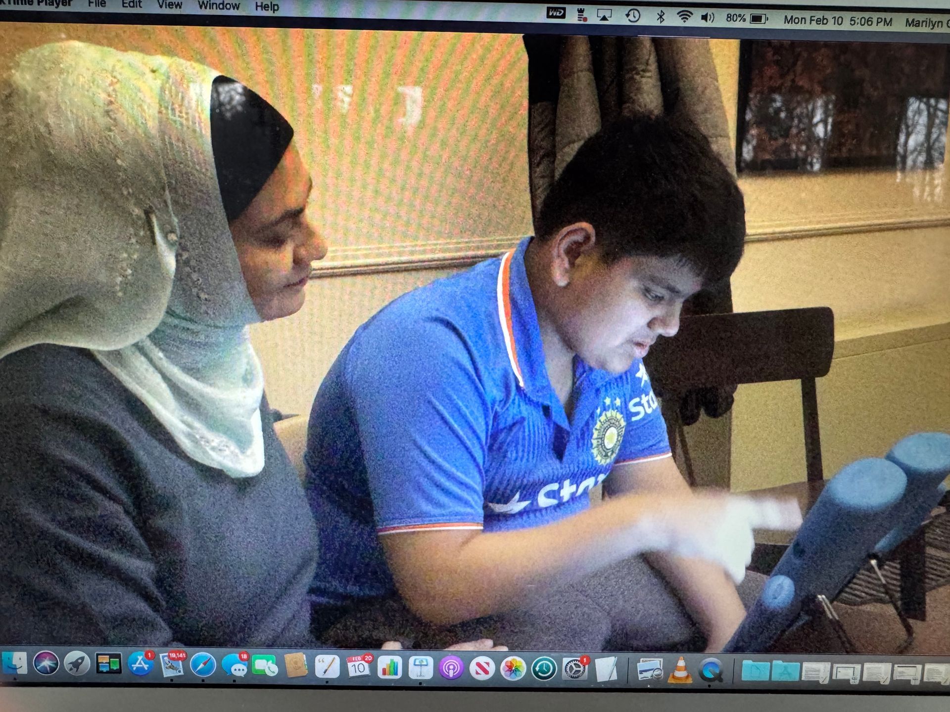 Woman in hijab helps boy in blue shirt with a tablet indoors.
