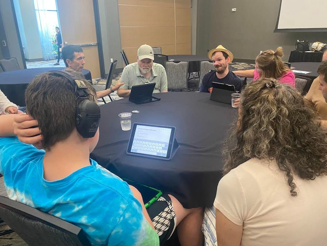 People gather around a round table in a meeting, using tablets.