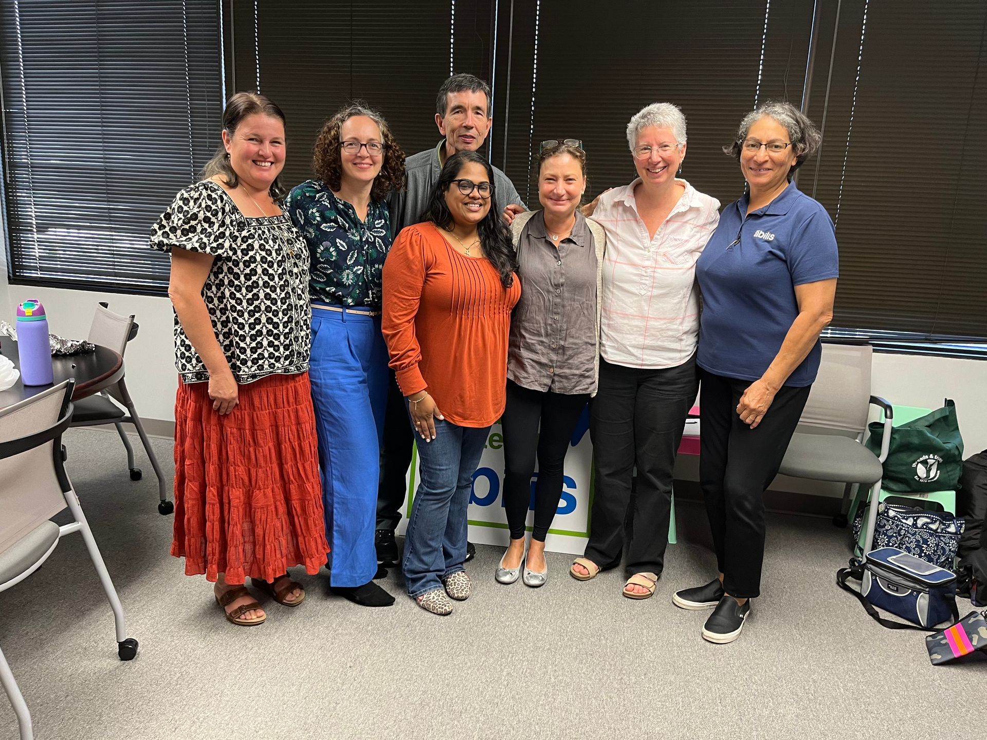 Group of eight people smiling, posing together indoors.