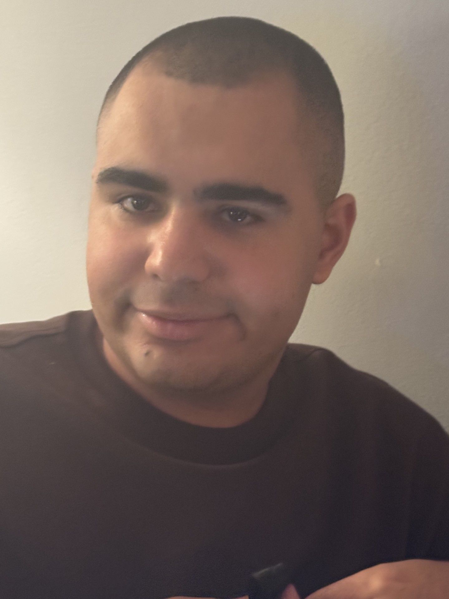 Man with short dark hair and a light complexion smiling, wearing a white t-shirt, indoors.