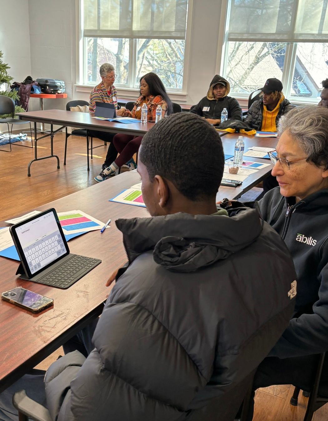 People at a table working with tablets, papers. A group discussion in a brightly lit room.