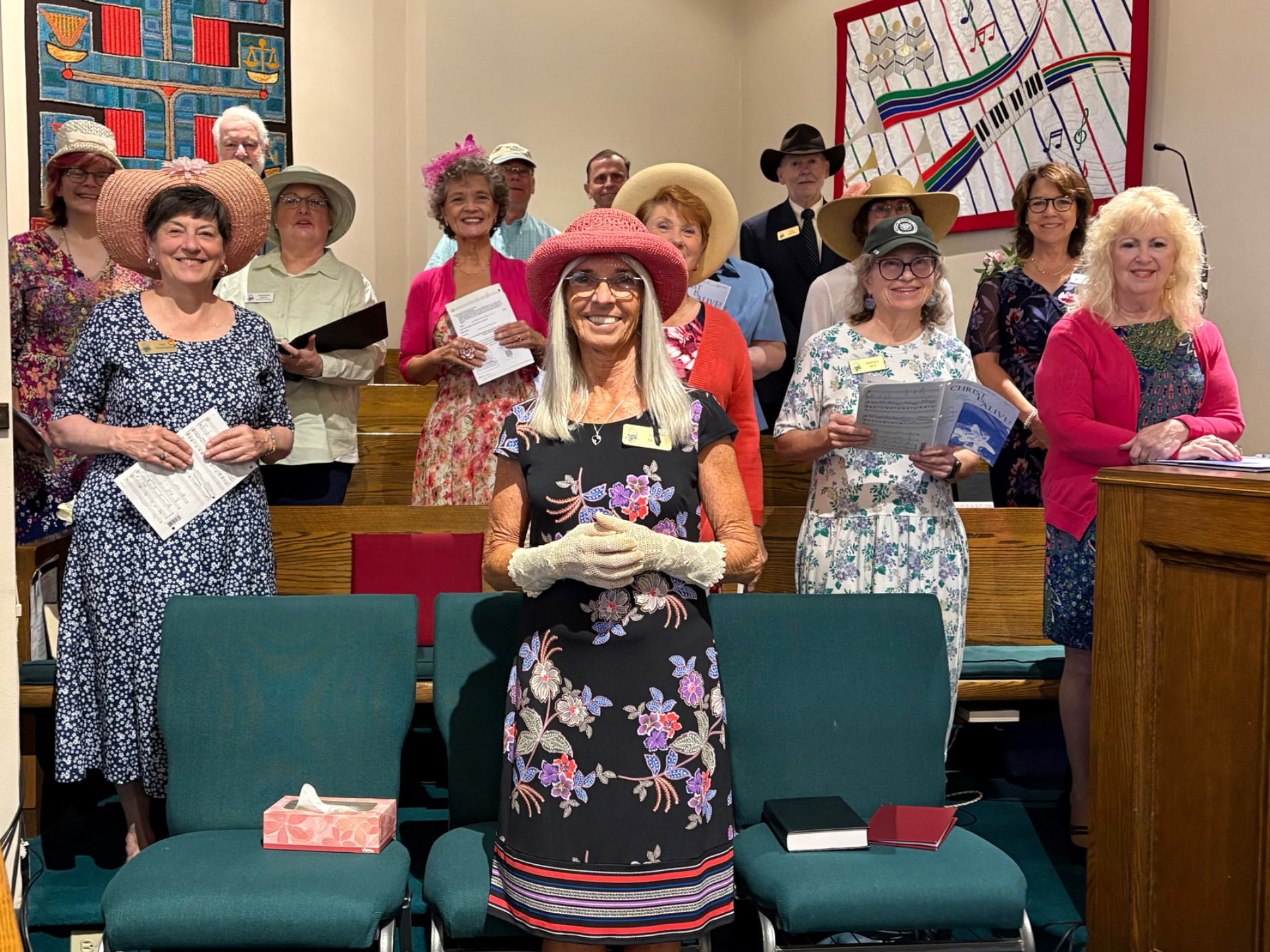 Group of people wearing hats in a church pew; some holding papers.