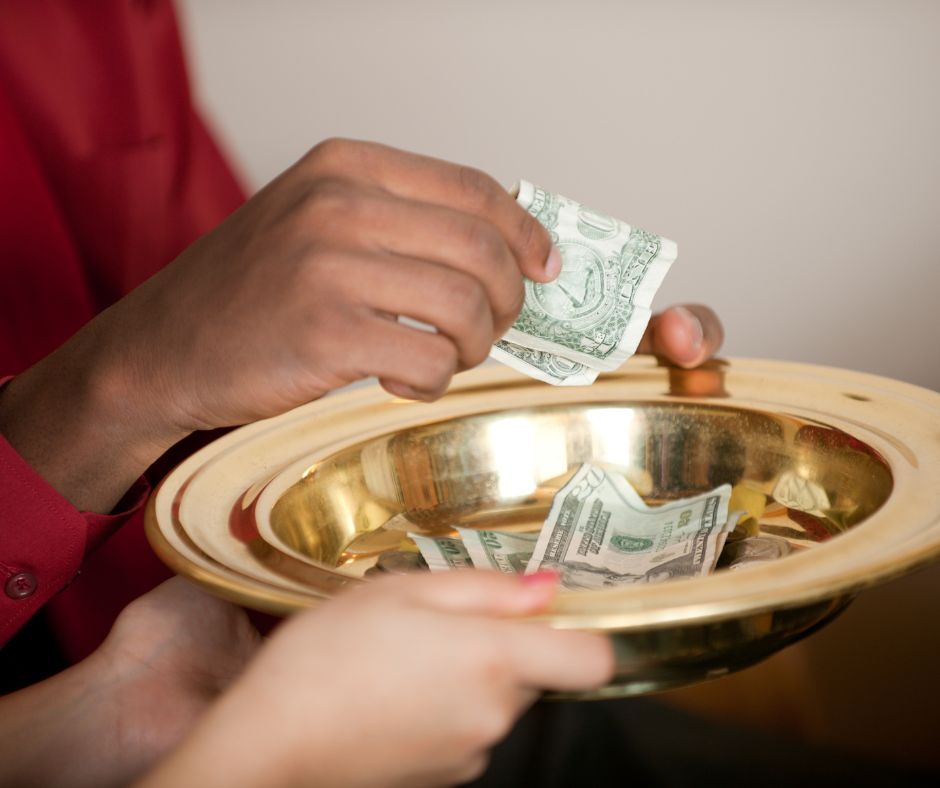 Person placing money in a golden donation bowl held by another person. Red shirt visible.