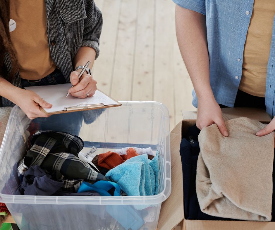 Two people sorting clothes, one writing on a clipboard, the other packing a box.