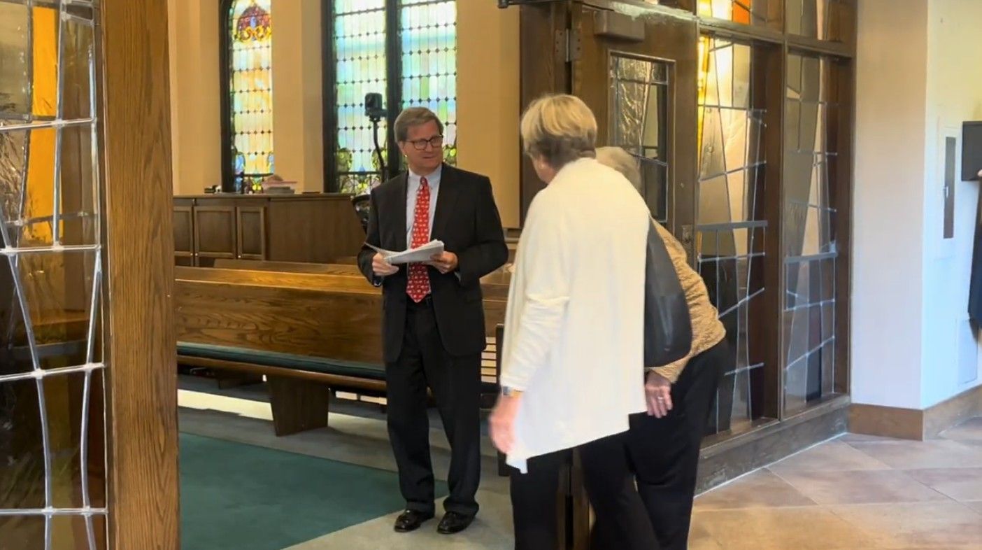 A man in a suit speaks to two women near an interior church entrance.