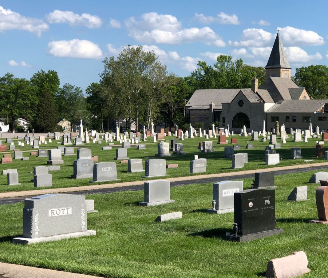 Cemetery with gravestones and a church building with a steeple under a blue sky.