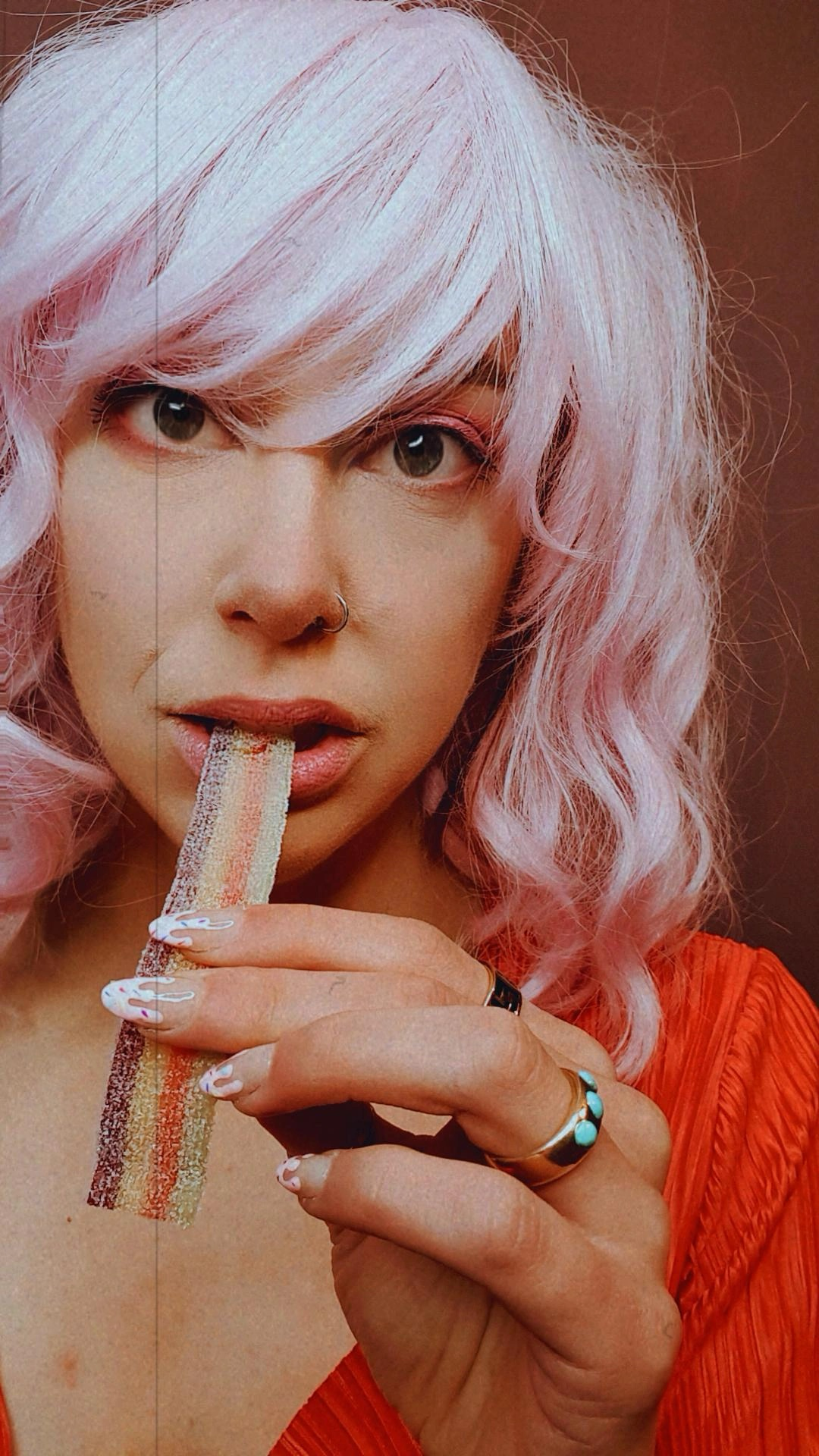 A woman with pink hair is eating a piece of candy.