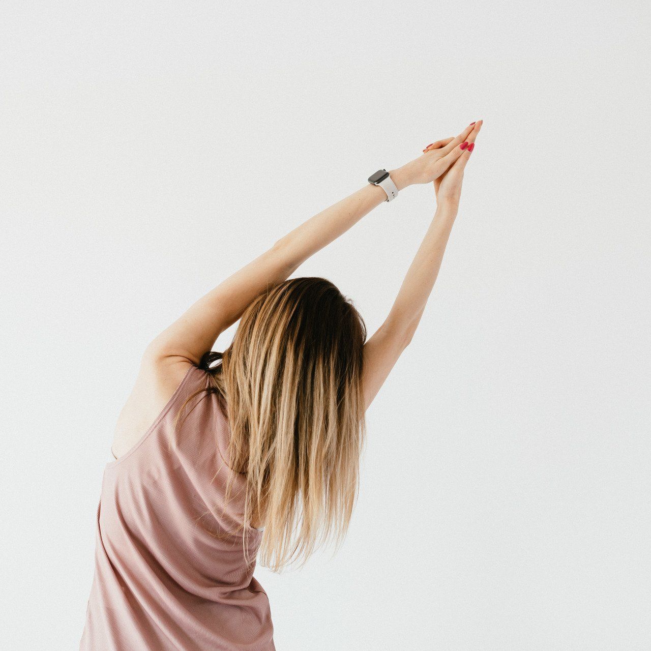 A woman in a pink shirt is stretching her arms over her head.