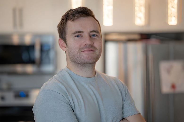 Man painting a white wall, standing in a room with a window.