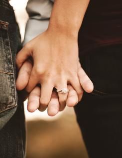 Two people holding hands, one wearing an engagement ring.