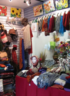 Colorful boutique interior with hanging scarves, sweaters, hats, and folded knitwear on display.