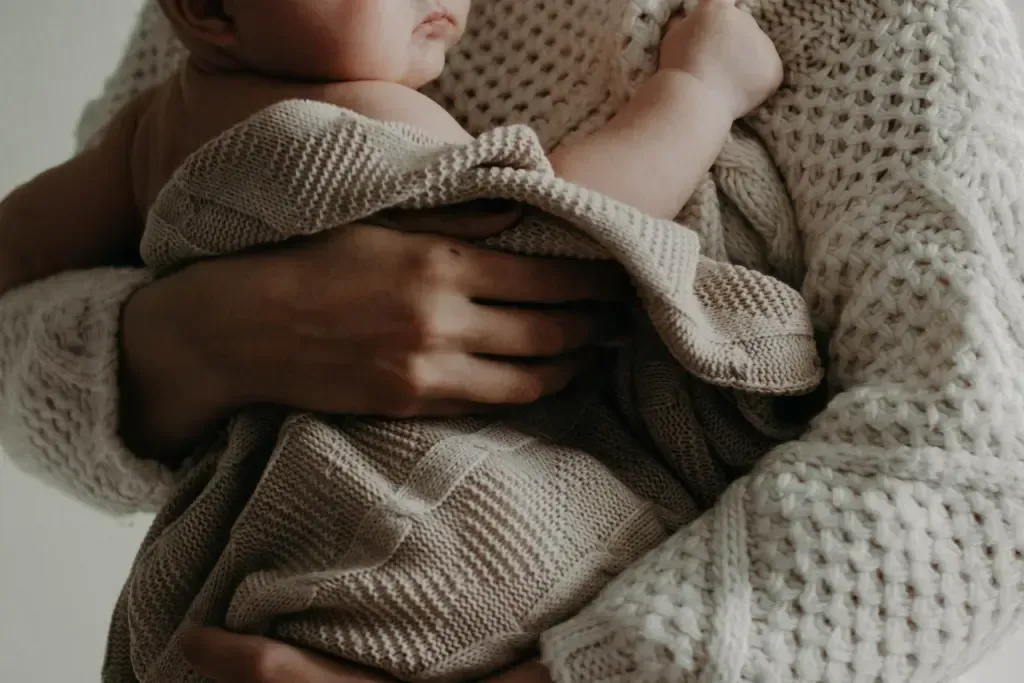 A woman is holding a baby wrapped in a blanket.