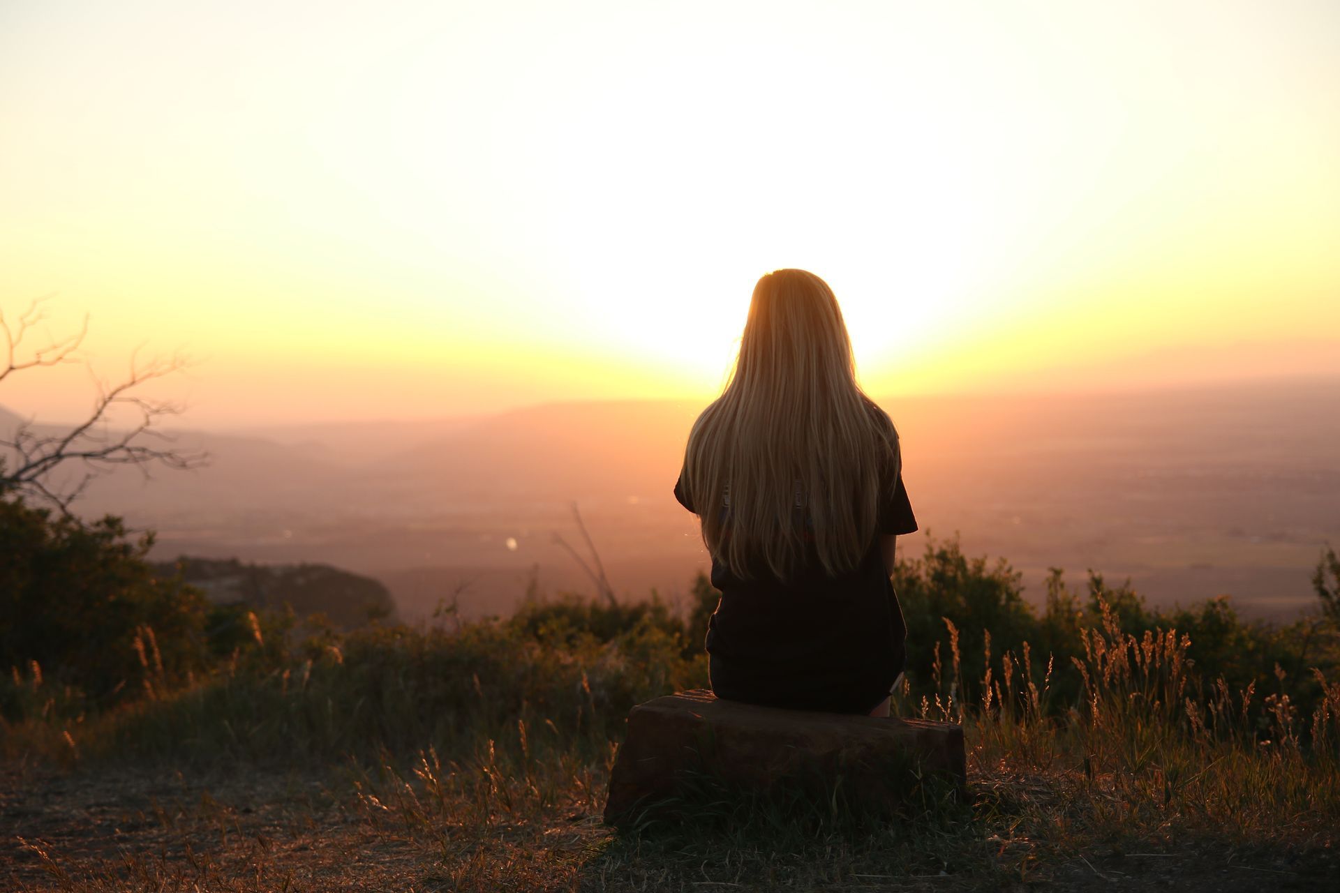 A woman is sitting on a rock looking at the sunset.