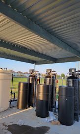 Outdoor water filtration system under a metal roof; several large tanks in an open field.