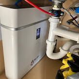 White water filtration system under a sink, connected to plumbing and red tubing.