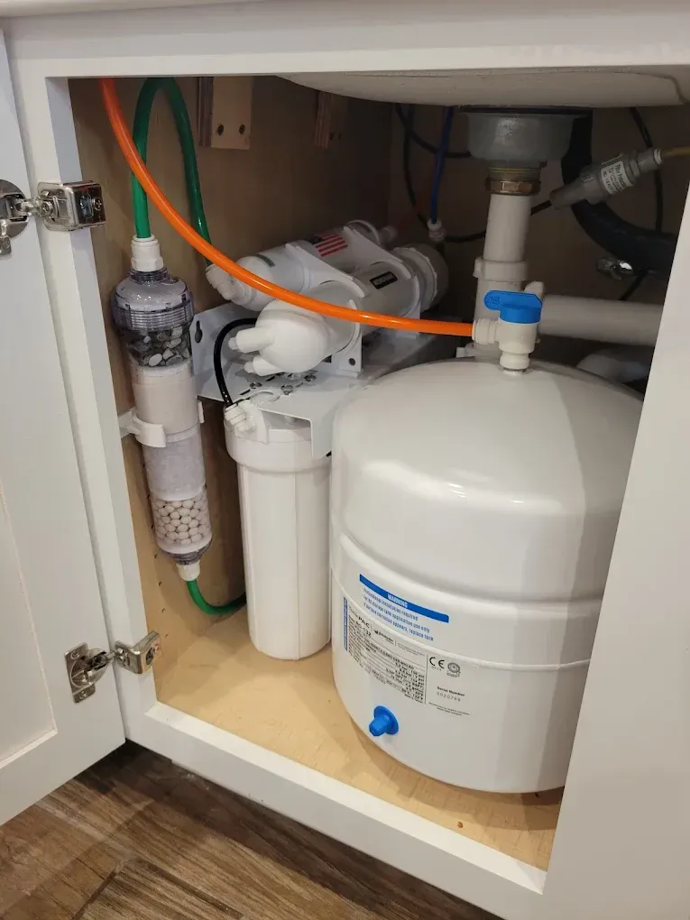 Under-sink reverse osmosis water filtration system: white tank, filters, and tubing inside a cabinet.