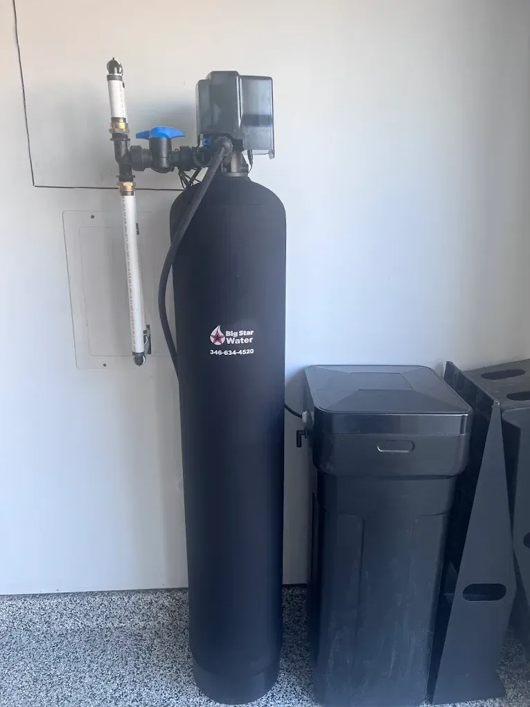 A water softener system in a garage, with a black tank and a salt container.