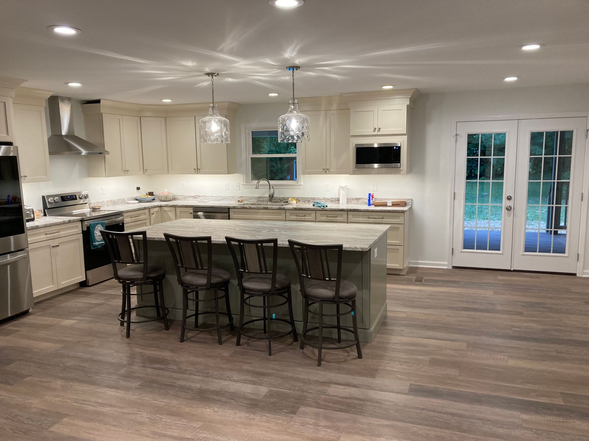 A kitchen with white cabinets , granite counter tops , stainless steel appliances and a large island.